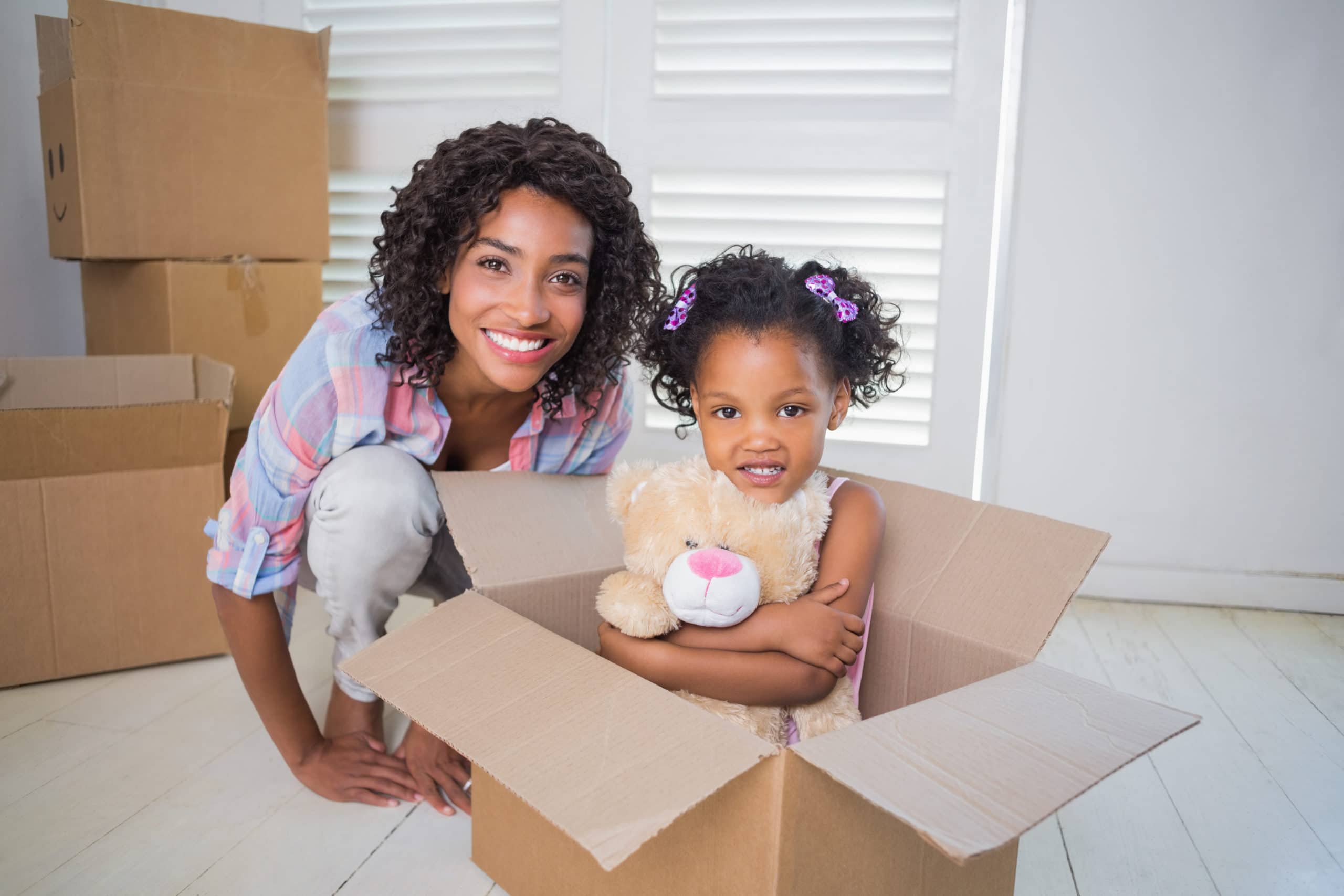 Cute daughter sitting in moving box with mother in their new home
