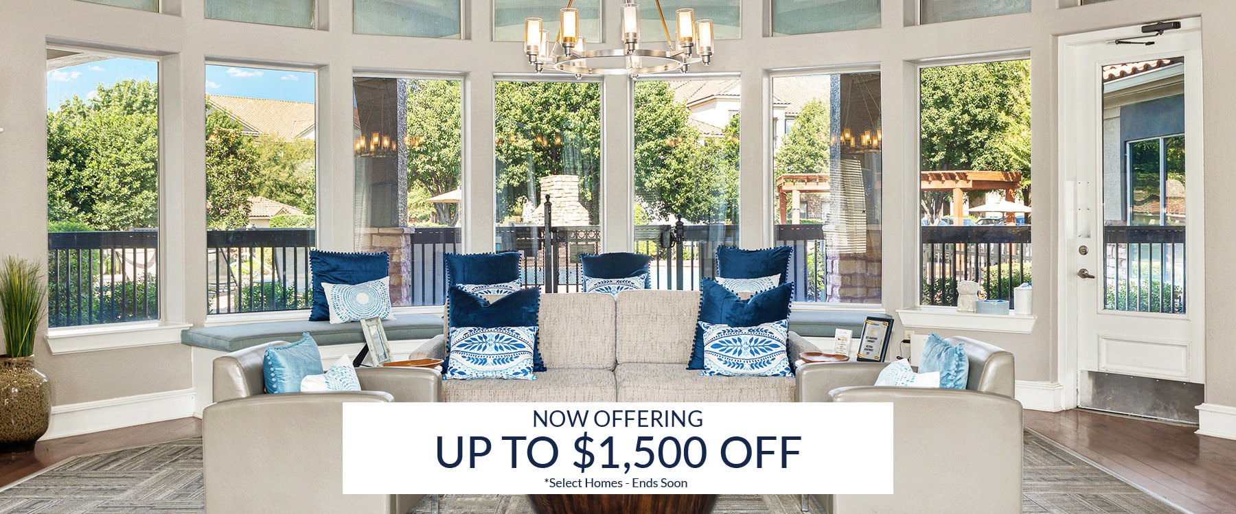 Modern apartment clubhouse with large windows, blue and white decor, and a sign offering up to $1,500 off select homes.