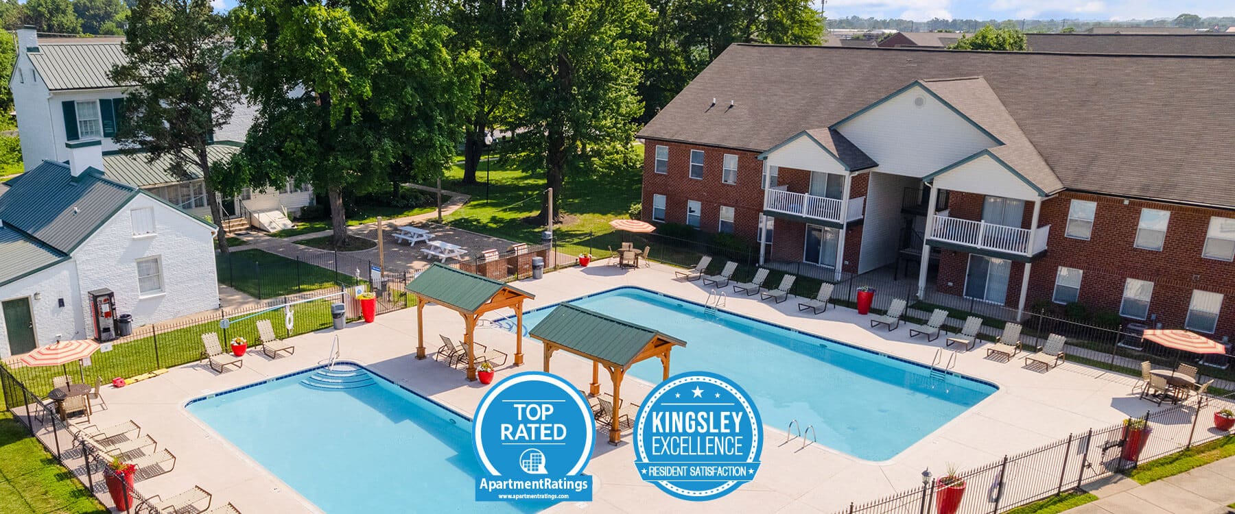 Aerial view of an apartment complex pool area with lounge chairs, umbrellas, and two award badges displayed in the foreground, capturing a relaxing scene reminiscent of Clearwater Farm serenity.
