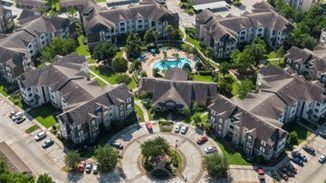 An aerial view of an apartment complex featuring multiple buildings surrounding a central community pool.